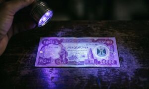 UV flashlight testing a genuine Iraqi Dinar note to check security features before you buy Iraqi Dinar online